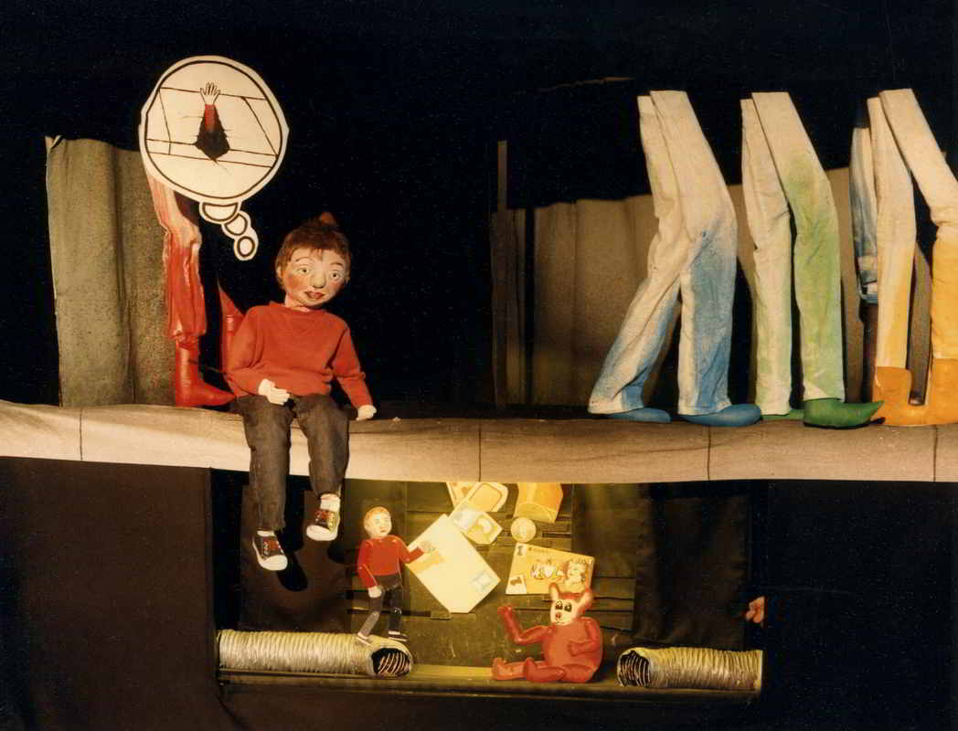 Streetwise Handspan Theatre Boy puppet sitting on pavement with legs with toy theatre scene of boy, bear and rubbish below ground