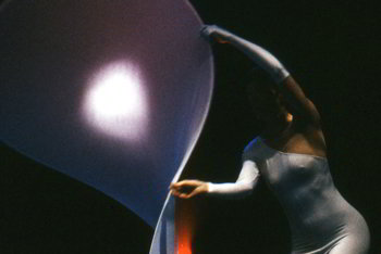 woman in shiny white leotard gracefully bending a large disc made of elastic white fabric stretched on a flexible circular frame