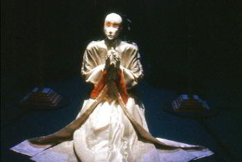 life-size white figure in white ceremonial robe kneels in prayer