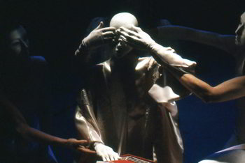 puppeteers place their white-gloved hands over the white figure's eyes