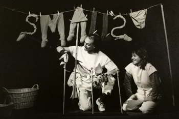 clothesline hung with items spelling the word Smalls behind man and woman with miniature clothesline