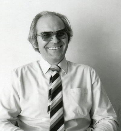 Handspan Theatre Alistair Stevenson portrait of seated, smiling man in business shirt and striped tie