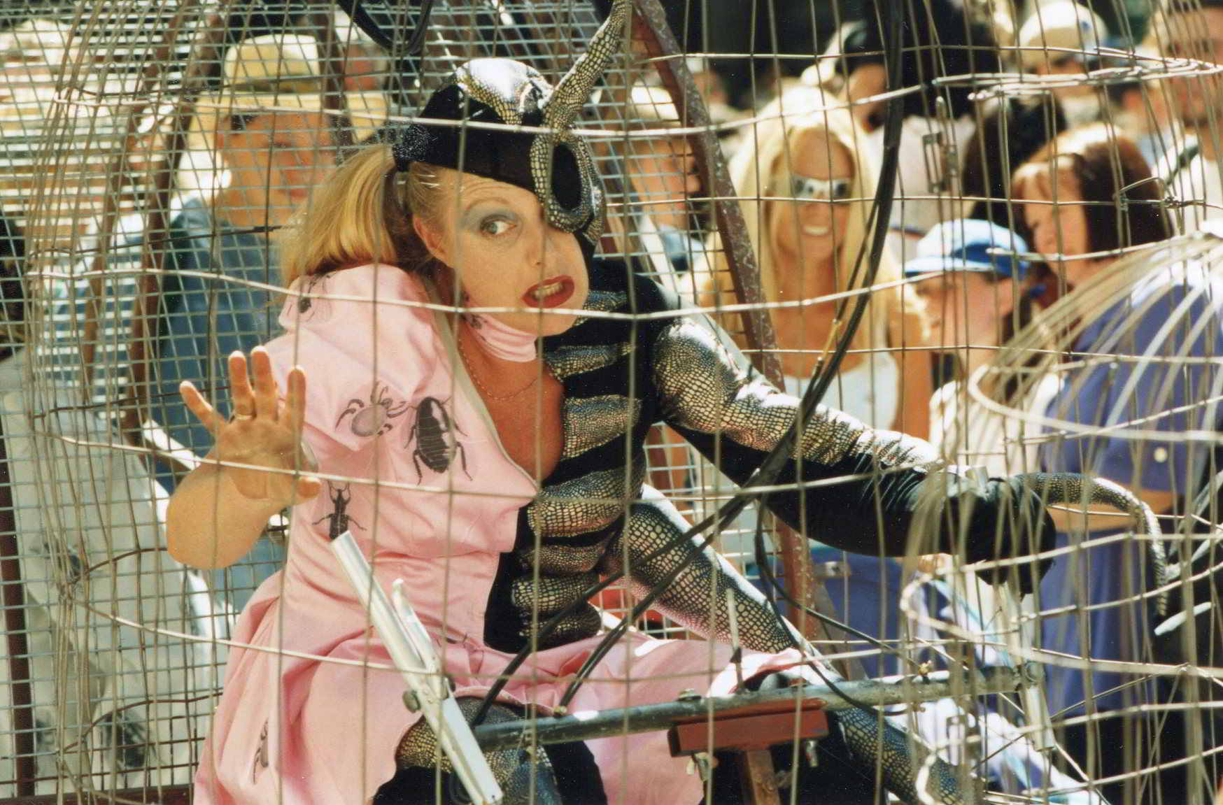 Road Roach strret theatre image a close up actor in dual costume pink dress and black and silver insect, inside a cage