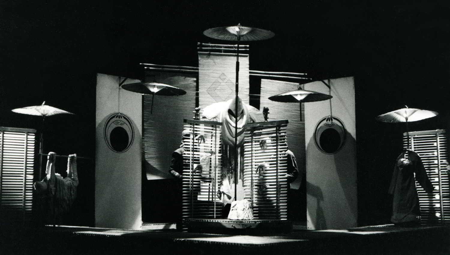 Handspan Theatre Nigel Triffitt's Secrets stage set with 5 hanging parasols over light squares & venetian blinds, central monk-like head & ship sails