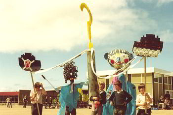 six children with their puppets - larger than life black man and white man, two representations of the local aluminium smelter and a big question mark